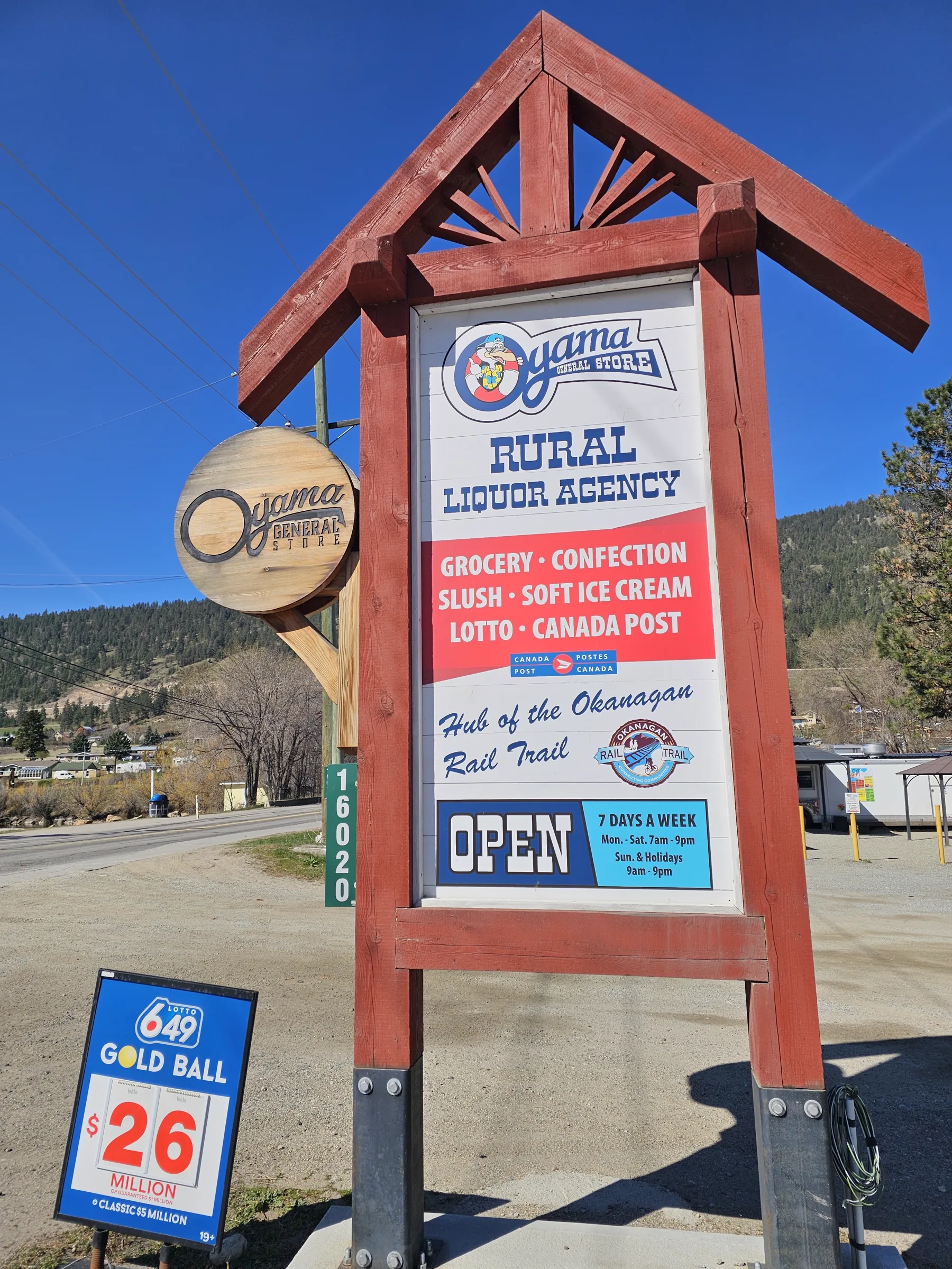 Roadside sign for Oyama General Store listing the rural liquor agency, groceries, soft ice cream, lotto and Canada Post