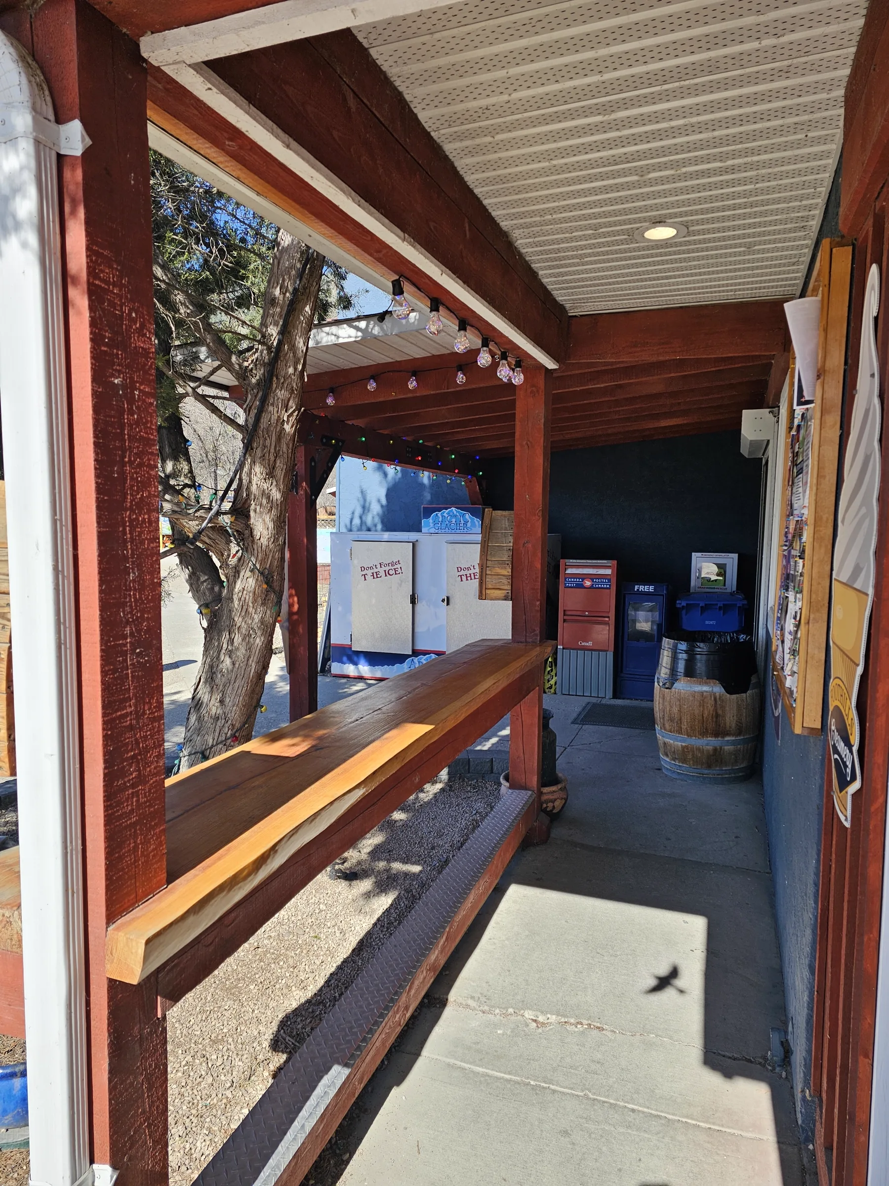 Shaded store breezeway with a wooden bench, Canada Post box and water station