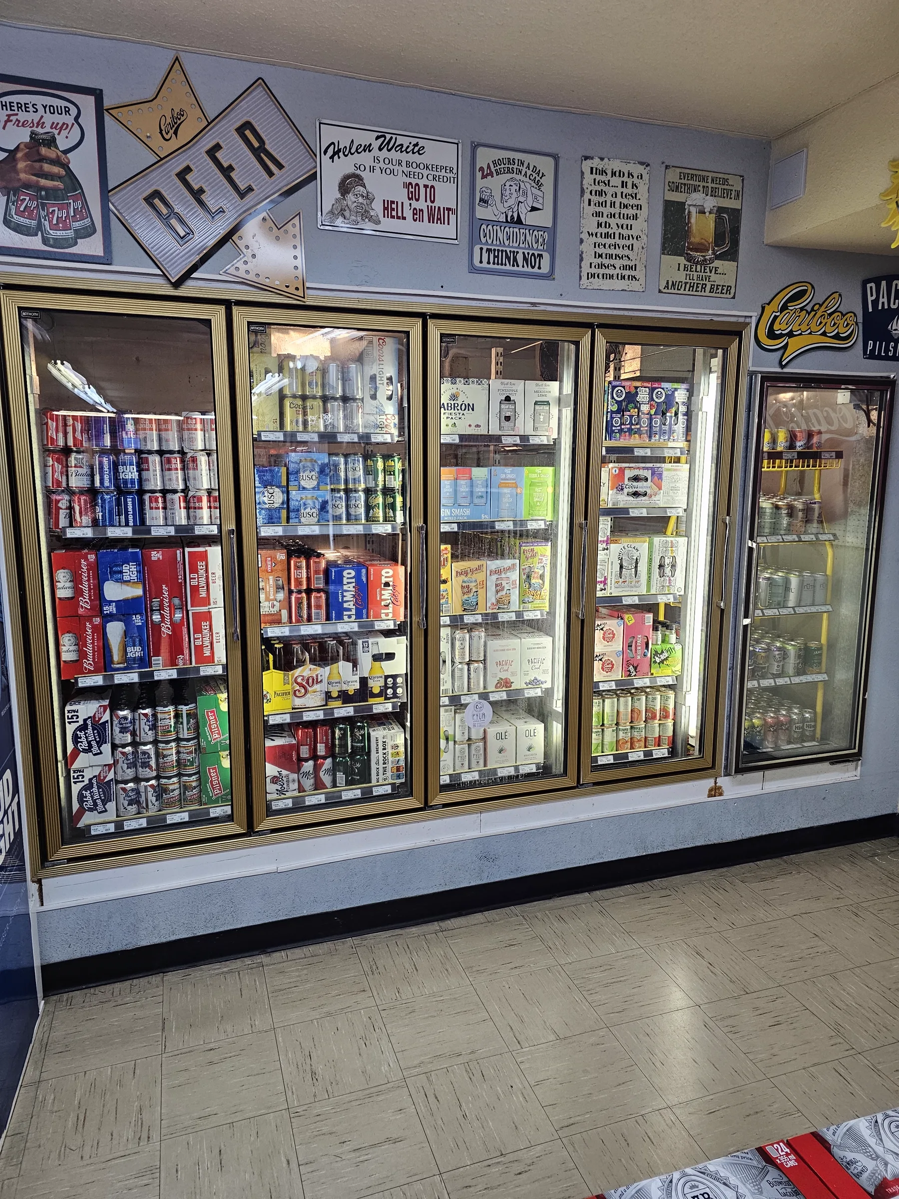 Wall of beer fridges filled with cold cans and bottles below vintage signs