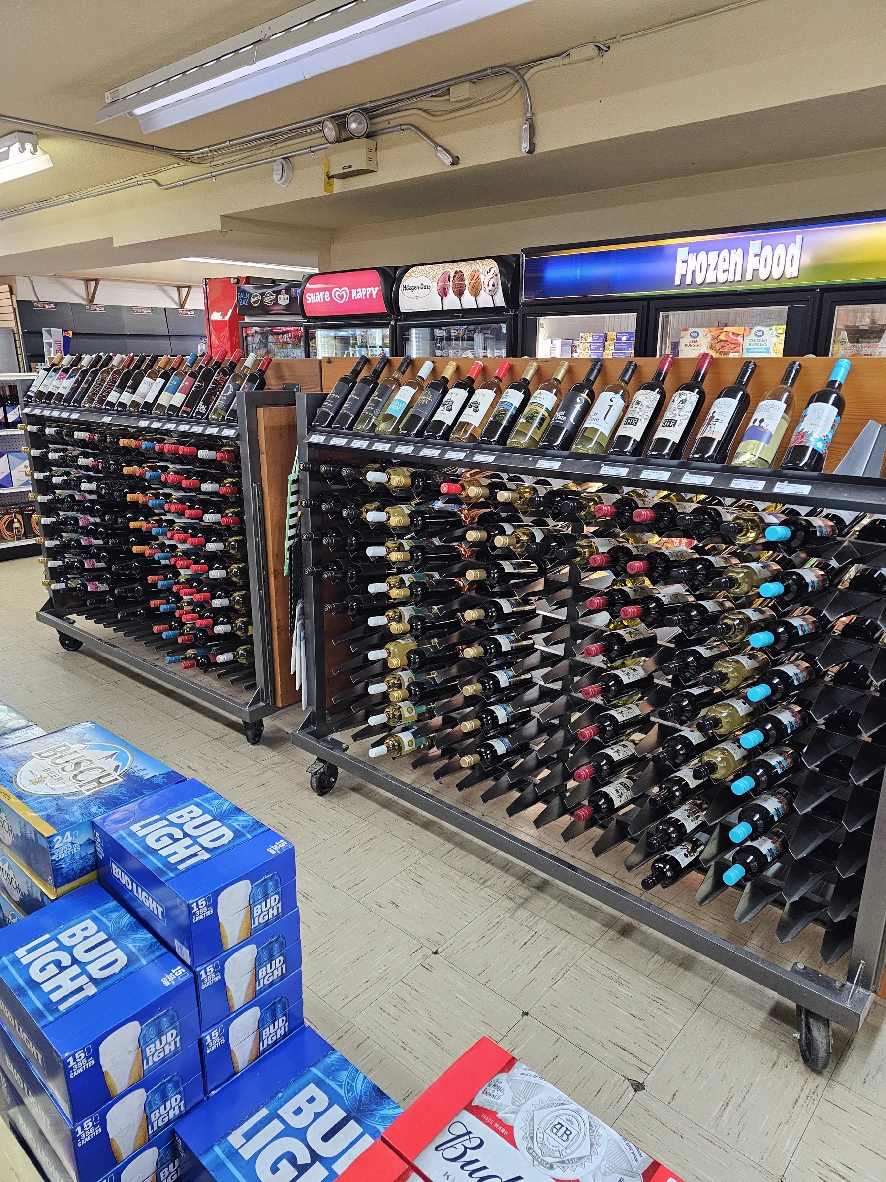 Wine racks full of bottles next to the frozen food cases and stacked beer